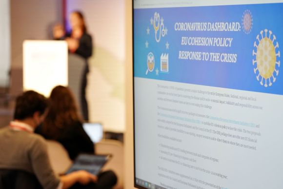 A sign in the foreground showing information about covid and cohesion policy, speaker in the background